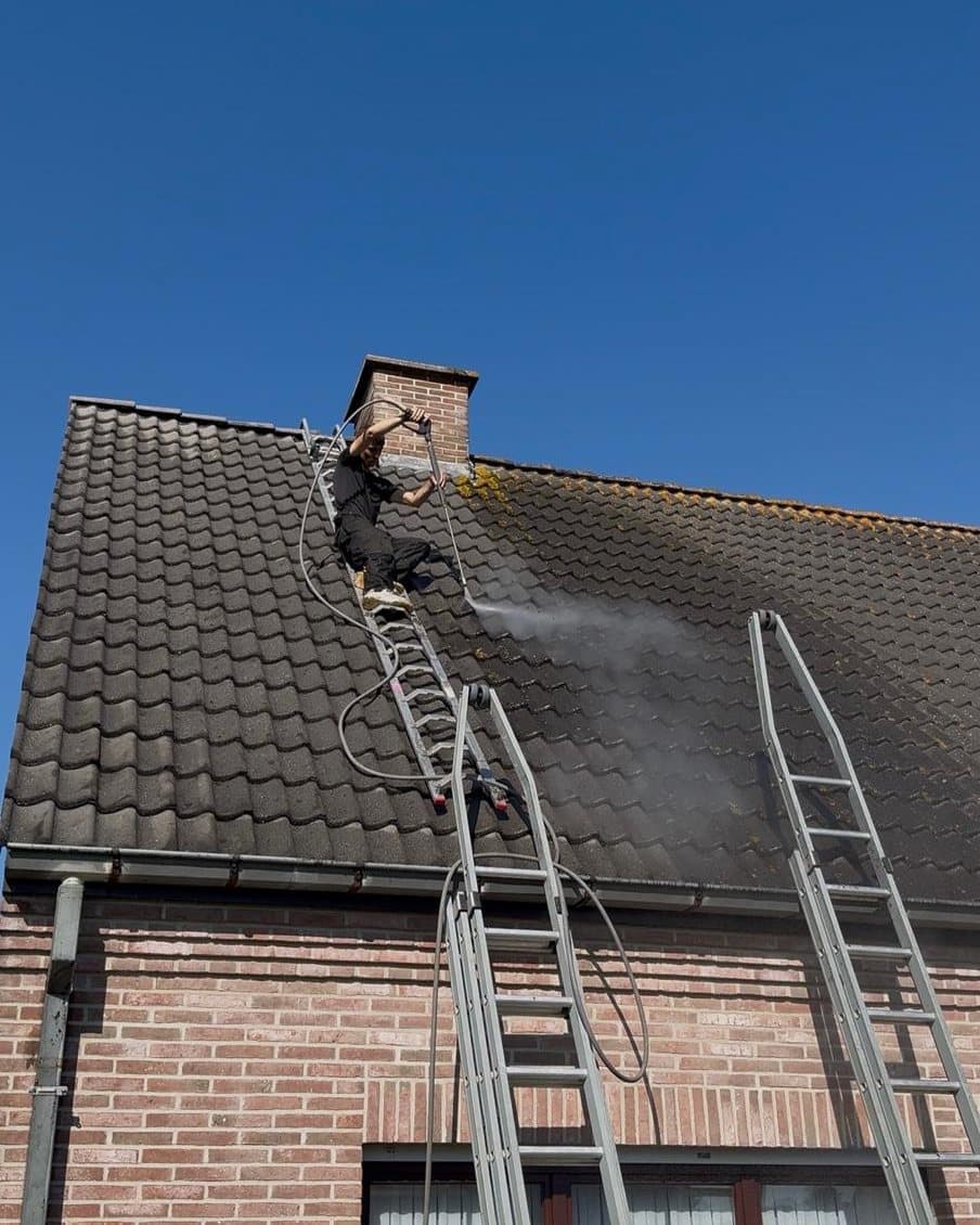 Dakreiniger verwijdert mos van een pannendak met ladders en een hogedrukreiniger