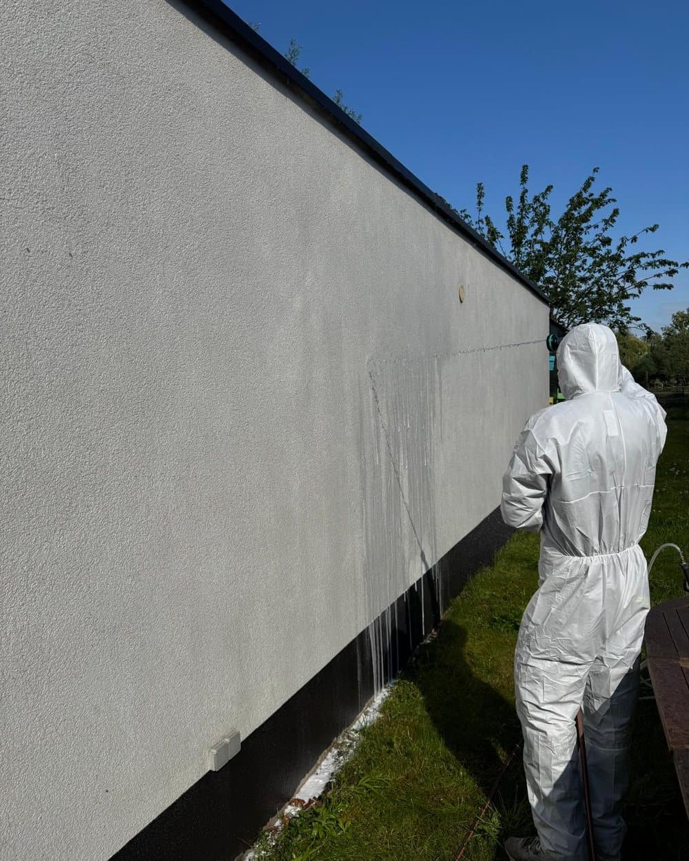 Gevelreiniger in beschermpak sproeit een bepleisterde gevel in